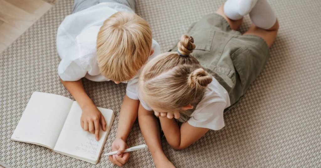 Cover nuovo articolo di blog: due bambini appoggiati al pavimento guardano insieme un quaderno di appunti